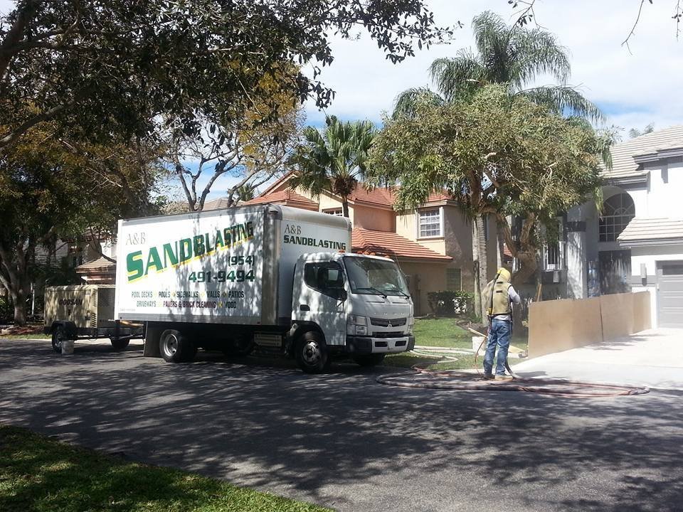 A&B Sandblasting truck in front of a South Florida home while a crew member blasts the driveway